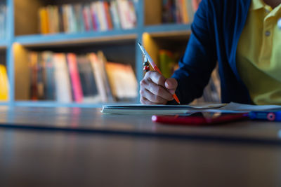 Midsection of person writing in book on table at library