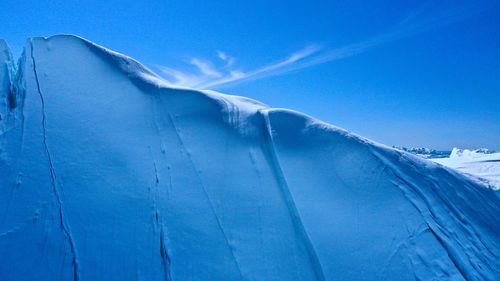 Low angle view of snow covered mountain against blue sky