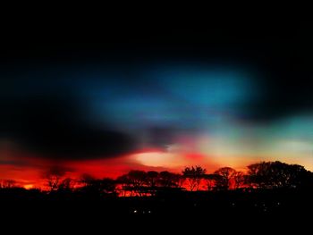 Silhouette trees against dramatic sky at sunset