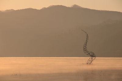 Metal sculpture in lake against silhouette mountain during sunset