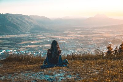 Rear view of woman sitting on field against sky