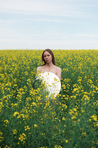 Rear view of woman standing amidst yellow flowering plants on field against sky