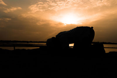 Silhouette man relaxing by lake against sky during sunset