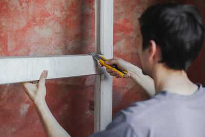 Caucasian male builder cleans a window frame with a construction knife.