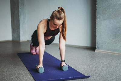 Woman exercising with dumbbells against wall