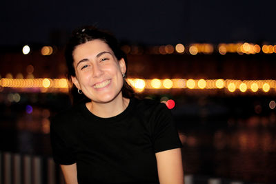 Portrait of young woman standing against illuminated city at night