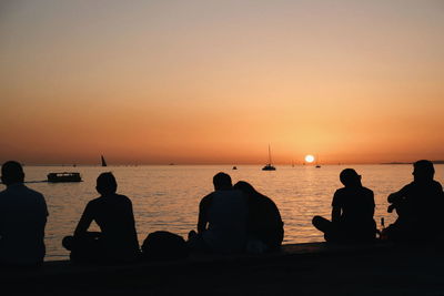Silhouette people sitting at beach against clear sky during sunset