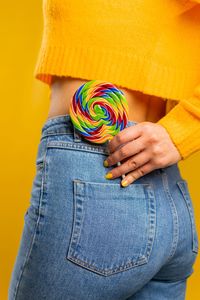 Midsection of woman with lollipop in pocket against yellow background