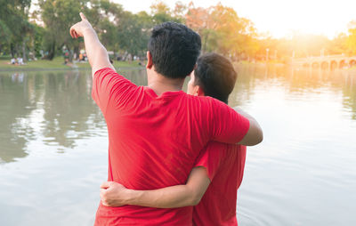 Rear view of homosexual couple standing by lake during sunset