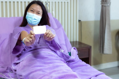 Portrait of woman holding mobile phone while relaxing on bed at home