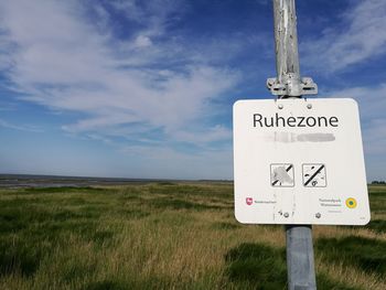 Road sign on field against sky