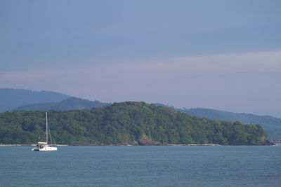 Sailboat sailing on sea by mountains against sky