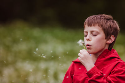 Boy blowing dandelion flower in forest