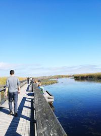 Rear view of man on lake against clear blue sky