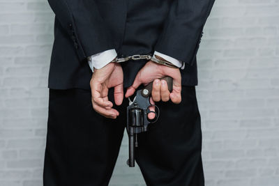 Midsection rear view of businessman with handcuffs holding gun