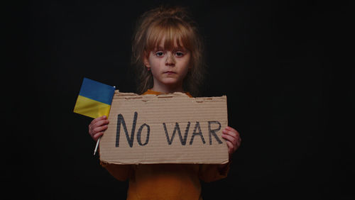 Portrait of boy holding paper against black background