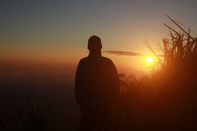 Silhouette man standing on field against sky during sunset