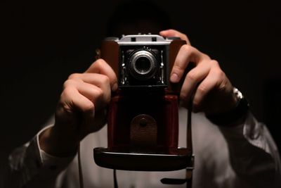 Midsection of man photographing through vintage camera against black background