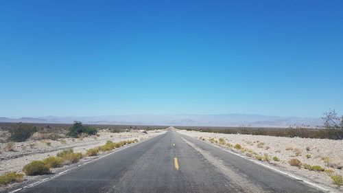 Empty road along landscape against clear blue sky