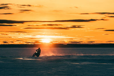 Motocrosso on frozen lake against sky during sunset