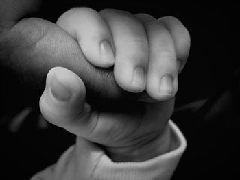 Cropped hand of baby holding human finger