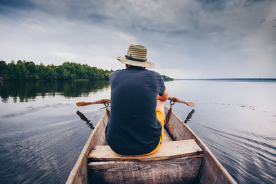 Rear view of man sitting on boat over lake against sky