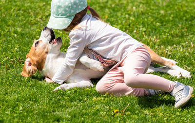 Happy little girl playing with beagle dog in garden.