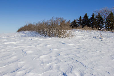 Snow covered land against clear blue sky