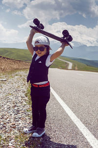 Fashionable child boy in white cap sneakers and vest stands with skate, road in mountains everest