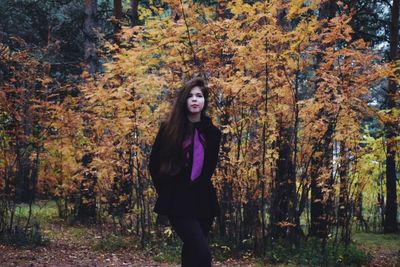 Portrait of young woman standing in forest during autumn