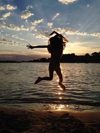 Full length of silhouette woman jumping on beach against sky