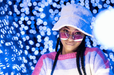 Joyful woman of color with a white beanie braided hairstyle and pink glasses enjoying the christmas