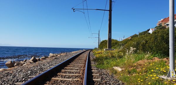 Railroad tracks by sea against clear blue sky