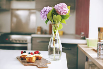 Fresh muffins with cream and berries are on the table in the kitchen, next to a bouquet of pink