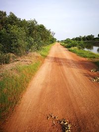 Dirt road along trees on field against sky