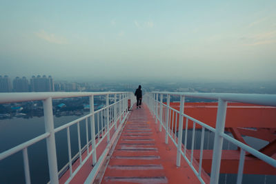 Man walking on railing over river against sky