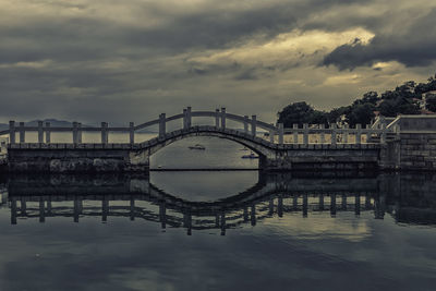 Arch bridge over river against cloudy sky