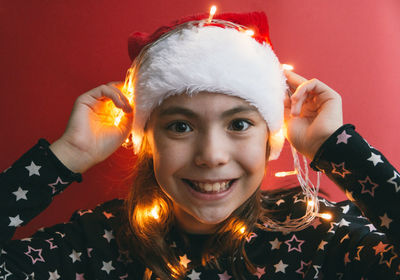Girl with illuminated string light against red wall