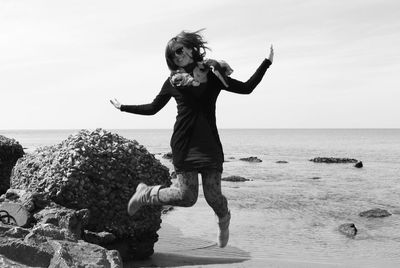 Full length of woman jumping at beach against sky