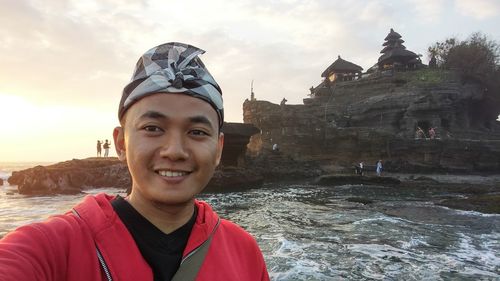 Portrait of smiling young man at beach against sky