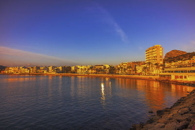 River by buildings against blue sky at sunset