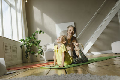 Mother helping girl on exercise mat at home