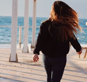 Rear view of woman standing at beach against sky
