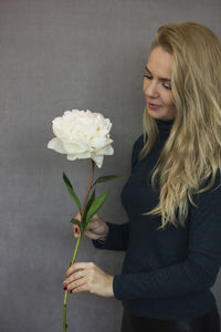 Woman holding white flower against gray wall