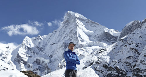 Low angle portrait of young man standing against snowcapped mountains