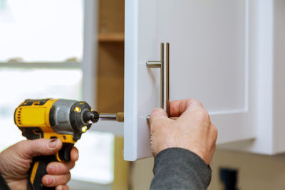 Cropped hand using nail gun on cabinet at home