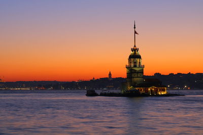 View of illuminated building by sea during sunset