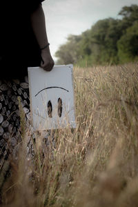 Midsection of man holding whiteboard while standing in field