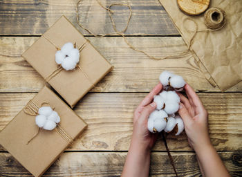 Women's hands hold a box on a wooden background.the decor is made of cotton flowers.