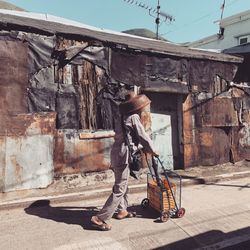 Full length of man with trolley walking on footpath against building